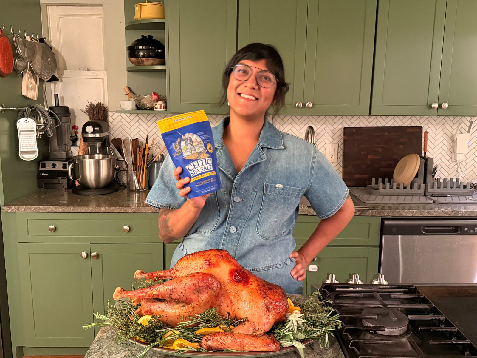 Sohla El-Waylly holding a Celtic Sea Salt Savory Brine Blend pouch beside a roasted turkey.